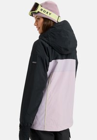 Suusajakk musta ülemine osa, helelilla alumine osa ja kontrastset kollast rõhku. Omab kapuutsi ja elastseid mansette. Roxy logo varrukal.