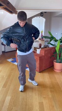 Mladić unutra nosi crnu puf jaknu, sive cargo hlače i bijele tenisice, prilagođavajući džep jakne.