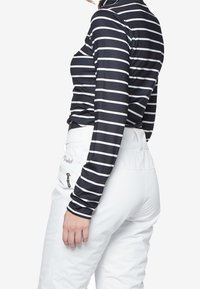 Donna che indossa una maglietta nera a maniche lunghe con strisce orizzontali bianche e pantaloni bianchi a vita alta con una tasca con zip sul lato.