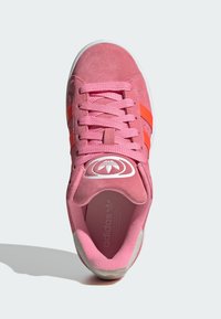 Sapatilha de camurça rosa com riscas laranja, atacadores texturizados e sola branca. Apresenta um logótipo circular na língua e um colarinho almofadado.