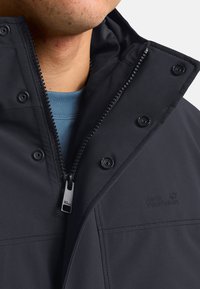 Giacca outdoor nera con colletto alto, chiusure a scatto e dettagli con zip. Presenta una texture morbida e un logo sul lato.