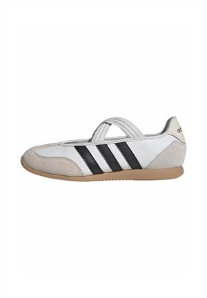 Sneaker bassa bianca e beige con strisce nere, cinturino elastico sulla parte superiore e suola in gomma, vista laterale su sfondo bianco.