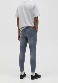 Jeans gris ajustados con un lavado desvaído, diseño de cinco bolsillos y parche de cuero en la parte posterior. Combinados con una camiseta gris de manga corta y zapatos negros.
