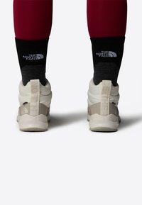 Hvit og beige høye sko med polstrede krager, med en teksturert såle. Svart og grå sokker med et logo over. Røde leggings.