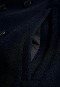 Marineblauwe wol stof met een zachte textuur, met een zijzakopening en knoopaccenten. De voering is van een contrasterende donkere kleur.