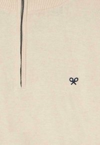 Suéter de punto beige con cuello de media cremallera y ribete azul marino. Presenta un pequeño logo azul marino que se asemeja a unas tijeras en la parte inferior izquierda.