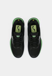 Čierne športové topánky s textúrovaným zvrškom, zelenými akcentami a bielymi podošvami. Jazyk má mriežkový vzor a logo.