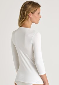 Witte, aansluitende top met lange mouwen en een ronde halslijn, zijaanzicht weergegeven, waarbij het naadloze ontwerp wordt benadrukt.