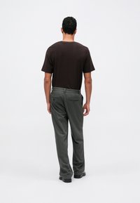 Brązowa, krótko rękawowa koszulka w połączeniu z ciemnozielonymi spodniami o prostym kroju. Spodnie mają tylne kieszenie i gładką fakturę materiału.