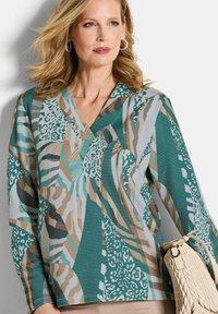 Kleurrijke patroon top met verschillende texturen, tinten van teal, beige en grijs, met een V-halsontwerp en een losse pasvorm. Aangekleed met een geweven handtas.
