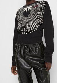 Černá krátká mikina s bílým geometrickým grafickým motivem a nápisy. Kombinováno s lesklými černými plisovanými kalhotami.