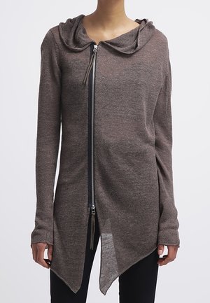 Brauner asymmetrischer Zip-Up-Cardigan mit Kapuze, getragen über schwarzen Hosen, gezeigt an einer Person von den Schultern bis zu den Hüften.