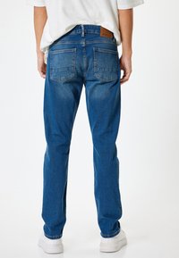 Jeans de mezclilla azul con un diseño clásico de cinco bolsillos, que presentan un parche de cuero marrón en la cintura y un corte recto.