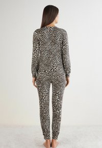 Leopardenmuster-Pyjama-Set in Beige und Schwarz, bestehend aus langärmeligen Oberteil und eng anliegenden Hosen, aus weichem, dehnbarem Stoff.