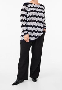Sweter z długim rękawem, w granatowo-białą koronkę, w falisty wzór, zestawiony z czarnymi szerokimi spodniami i czarnymi botkami na obcasie.