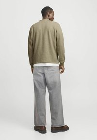 Olivengrüne, strukturierte Jacke mit langen Ärmeln, kombiniert mit hellgrauen, weiten Jeans. Braune Stiefel vervollständigen das Outfit.