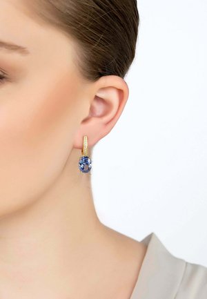 Orecchini a cerchio in oro con una superficie texture, caratterizzati da un grande gemstone ovale blu appeso sotto. Il montaggio è semplice ed elegante.