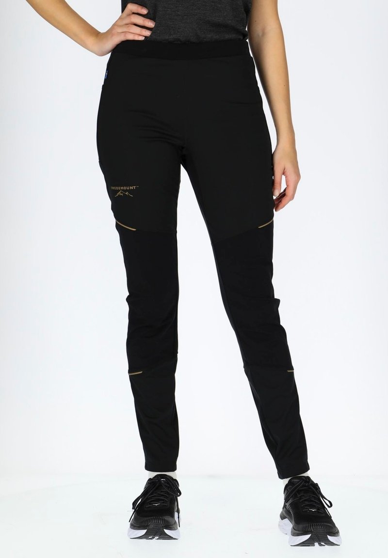 Black athletic pants with a slim fit, featuring contrasting fabric panels, a gold logo, and knee accents. Made from a lightweight, stretchy material.