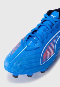 Blauer Fußballschuh mit einer strukturierten Synthetikoberfläche, roten und weißen Akzenten sowie einem gemusterten Design, ausgestattet mit schwarzen Stollen an der Sohle.