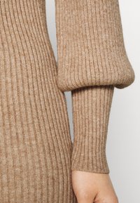 Beige ribbad stickad tröja med puffärmar och en figurnära design. Mjuk textur med en subtil lyster som förstärker den visuella djupet.