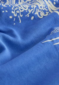 Blauer Stoff mit weißen abstrakten Blumenmustern, Nahaufnahme mit sichtbarer Textur und Falten.