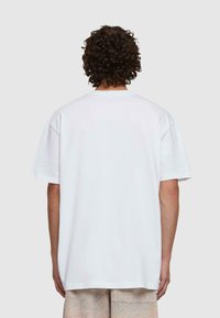 Bijela pamučna majica s okruglim izrezom i kratkim rukavima. Labav kroj, glatka tekstura i minimalni detalji. Vidljivi šavovi na ramenima.