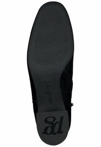 Zapato de ante negro con una suela lisa y ligeramente texturizada. Presenta un tacón bajo y un logo discreto en la parte exterior de la plantilla.