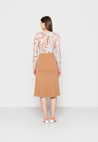A blusa de mangas compridas apresenta um padrão marmoreado em cores pastel; combinada com uma saia castanha sólida até ao joelho, de textura suave, e sandálias casuais.