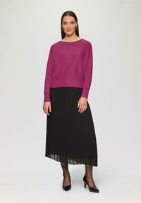 Fuchsia gebreide trui met geribbelde zoom, gecombineerd met een geplooide zwarte maxi rok. Zwarte hoge hakken maken de outfit compleet.