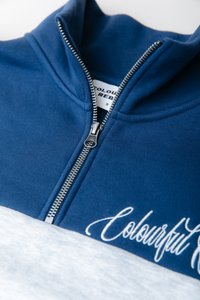 Navyblauwe zip-up sweatshirt met een witte ondersectie, voorzien van een metalen rits en een scriptlogo in het wit op de voorkant. Zachte stoftextuur.
