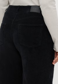 Zwarte corduroy broek met een textuurafwerking, voorzien van twee achterzakken en een leren merklabel aan de tailleband.
