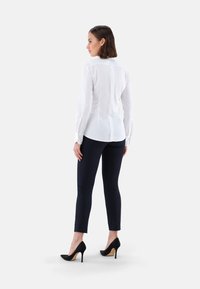 Weißes Langarm-Bluse mit einer Rückennaht-Detail, kombiniert mit dunkelblauen Slim-Fit-Hosen und schwarzen High Heels. Glatte Stofftextur.