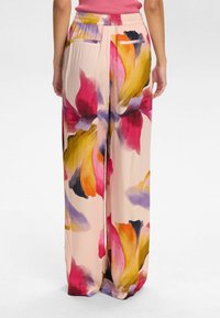 Pantaloni leggeri e svolazzanti di colore crema con vivaci motivi floreali in rosa, giallo e viola; dotati di una vita elastica e tasche posteriori.