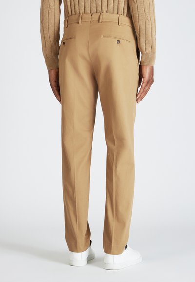 Pantalones beiges de tela suave con un diseño de pierna recta, que cuentan con bolsillos traseros dobles y un tobillo ligeramente ajustado. Usados con zapatillas blancas.