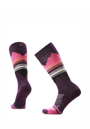 Een paar paarse sokken tot over de kuit met roze, oranje, zwarte en witte geometrische strepen en patronen, rechtopstaand weergegeven op een witte achtergrond.
