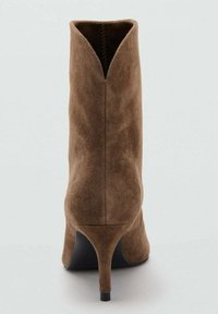 Botín de ante marrón con punta puntiaguda, tacón cónico y abertura en forma de V en la parte trasera. La textura es suave y lisa.