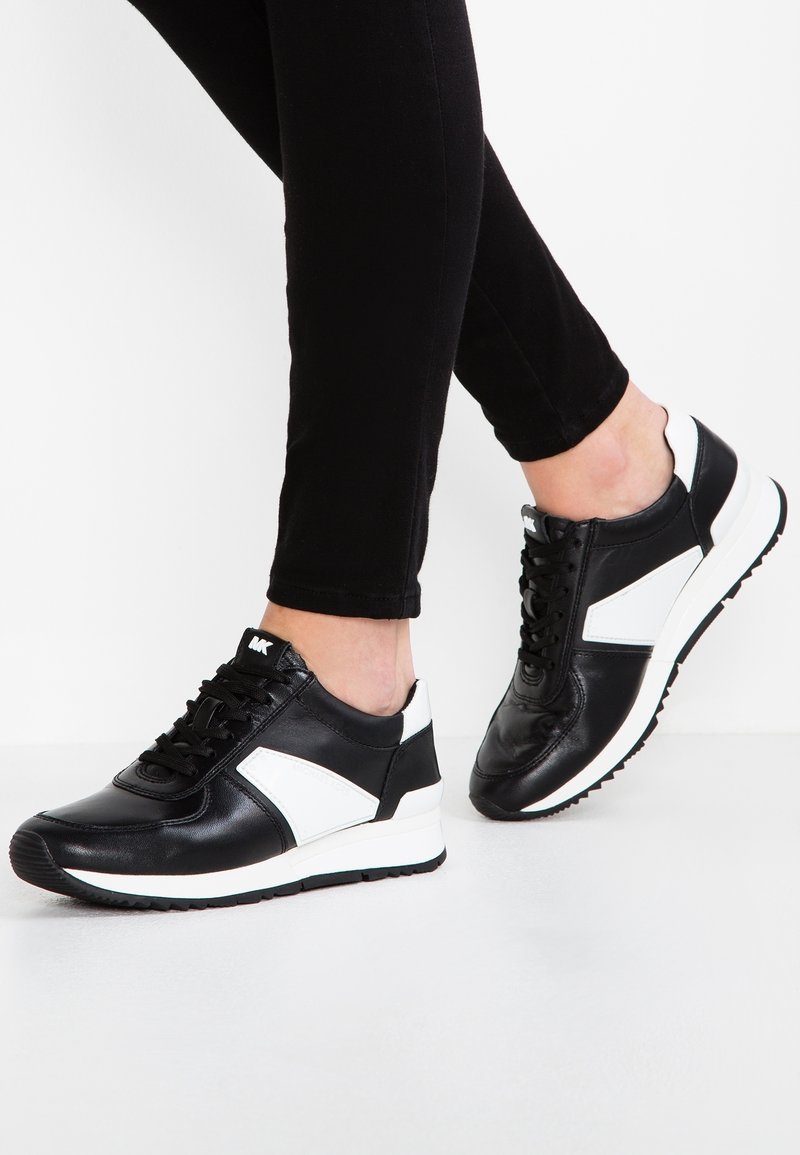 Černé kožené tenisky s bílými akcenty, s šněrováním, texturovaným povrchem a gumovou podešví. Klasický atletický styl.