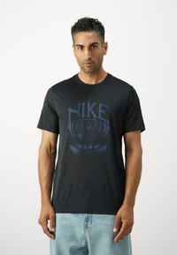 Must musta Nike t-särk, millel on sinine korvpalligraafika, ümmargune kaelus, lühikesed varrukad ja sile tekstuur. Minimalistlik disain koos logo detailiga.