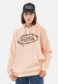 Sweat à capuche pêche avec une poche avant, des cordons de serrage et une impression de logo. Associé à une casquette noire avec un logo brodé blanc.