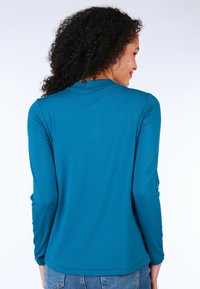 Türkises Langarmshirt aus glattem Stoff mit Rundhalsausschnitt, das ein dezentes Rückendetail und ein lässiges Design bietet.