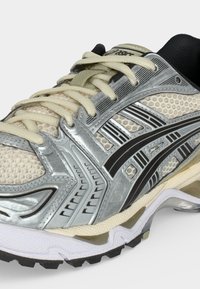 Ασημένιο και μπεζ παπούτσι τρεξίματος Asics με μαύρο σχέδιο ρίγας, υφασμάτινο πλέγμα με υφή, επενδεδυμένη σόλα και μπεζ κορδόνια.