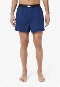 Navy blue cotton boxers with a button closure and elastic waistband featuring white logo detail. Standard fit, smooth texture.