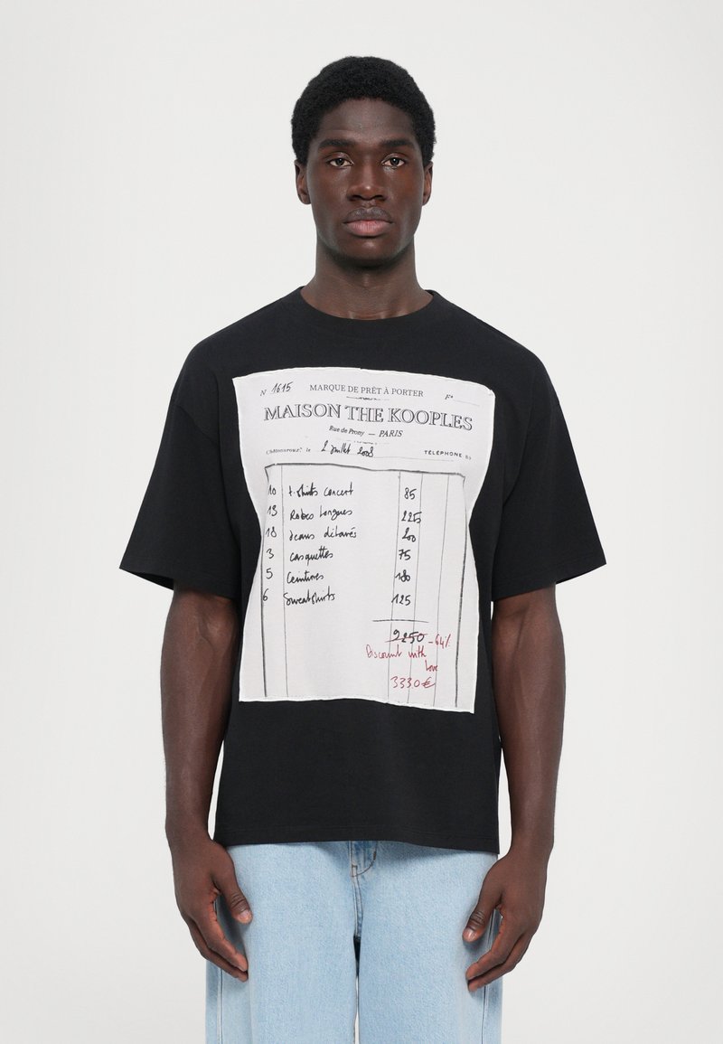 T-shirt en coton noir avec un design imprimé blanc comportant du texte tabulé et des notes manuscrites rouges. Coupe décontractée avec des manches courtes.