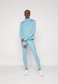 Lichtblauw sporttop met een hoge kraag en rits, gecombineerd met bijpassende leggings. Gladde stof en een aansluitend ontwerp, aangevuld met witte schoenen.