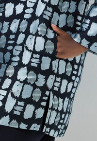 Tunica fantasia con base blu navy e disegni a pennellate azzurro chiaro, tessuto strutturato, tasca laterale e orlo con spacchi.