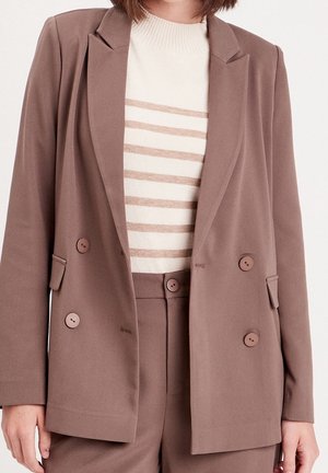 Blazer marron à double boutonnage en tissu doux, avec deux boutons, des revers pointus et des poches, porté sur un pull crème à rayures.