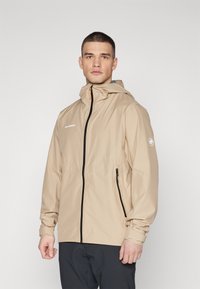 Beige vattentät jacka med frontdragkedja, justerbar huva och logotyp på bröstet. Har sidofickor och elastiska muddar.
