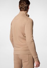 Pullover beige con collo alto, maniche lunghe e polsini a costine. Tessuto morbido, cuciture minime e design pulito.