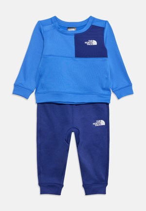 Kinder zweiteiliger blauer Trainingsanzug mit langärmeligem Oberteil und Hose, mit The North Face Logos auf Brust und Oberschenkel.
