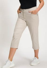 Beżowe spodnie 3/4 o gładkiej fakturze, z dwiema przednimi kieszeniami i zapięciem na zamek. Połączone z białymi sportowymi trampkami.